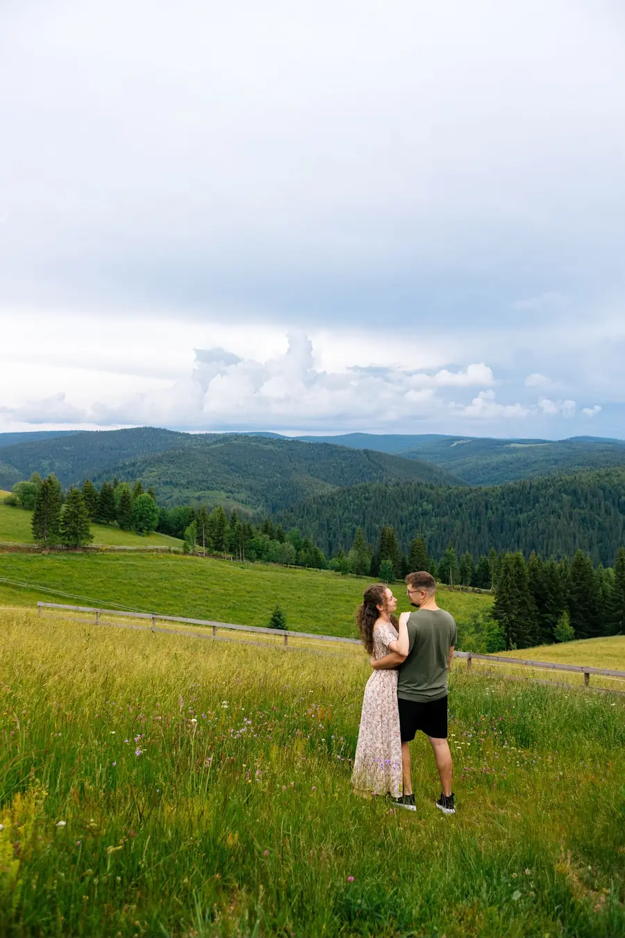 Couple in a mountain meadow with a view over the forested hills